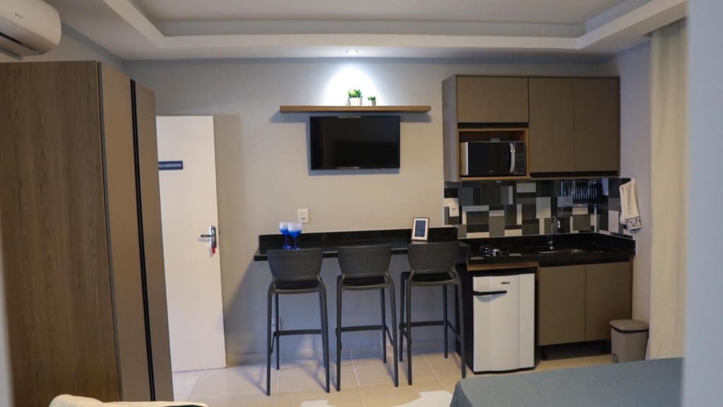 Cozinha completa de um flat com cooktop, micro-ondas, geladeira e bancada de granito