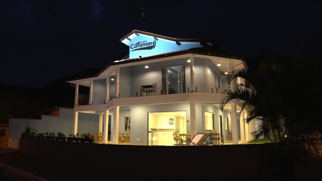 Fachada do Flats Catamarã iluminada à noite, com o letreiro aceso e a varanda de redes